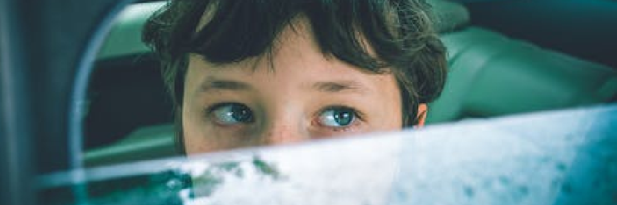 child with blue eyes looks through a car window
