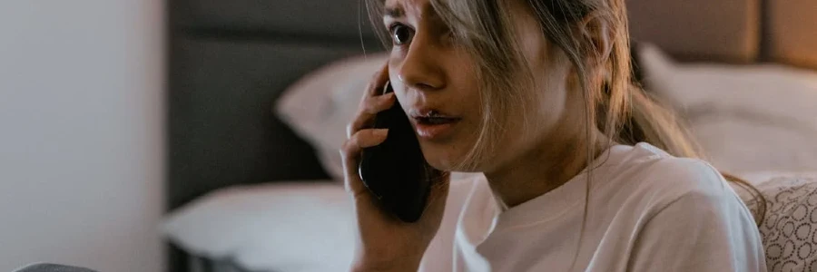 A worried woman in a white shirt making a distressing phone call indoors