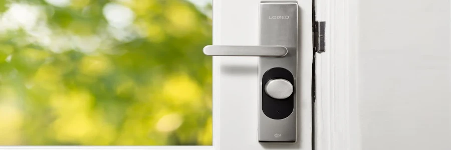 Sleek smart door lock on a white door with blurred green foliage in the background